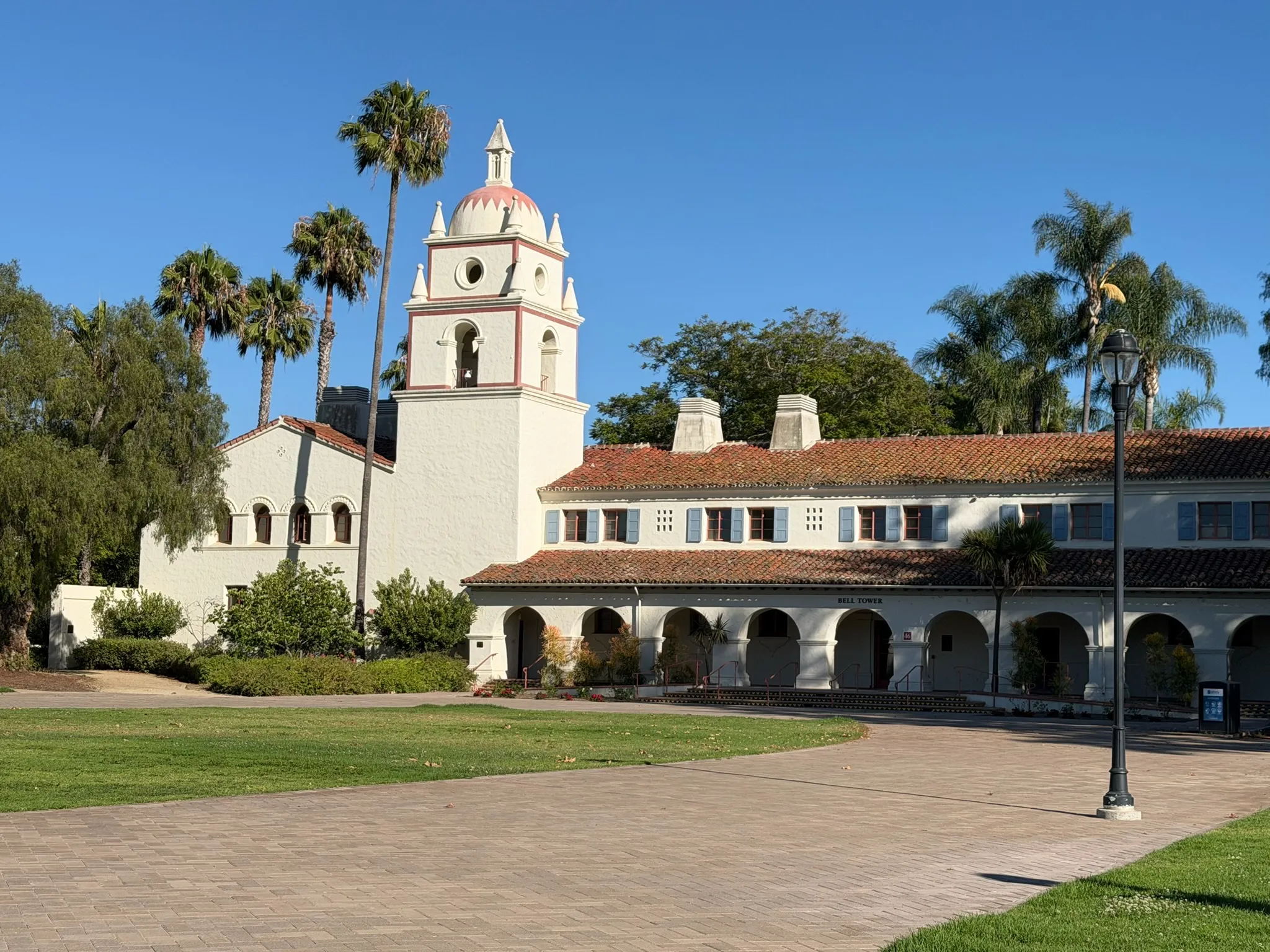 White mission church with bell tower, colonnade arches, and palms
